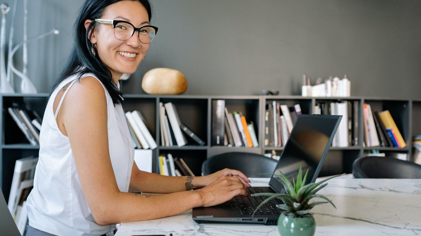 A smiling woman working on a laptop at a desk in a bright office