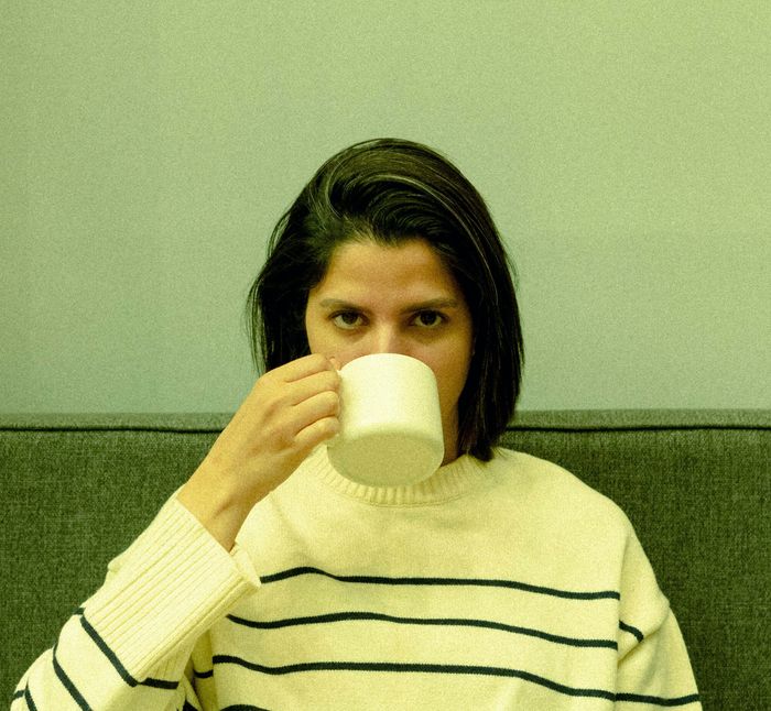 A young woman drinking from a white mug against a green wall